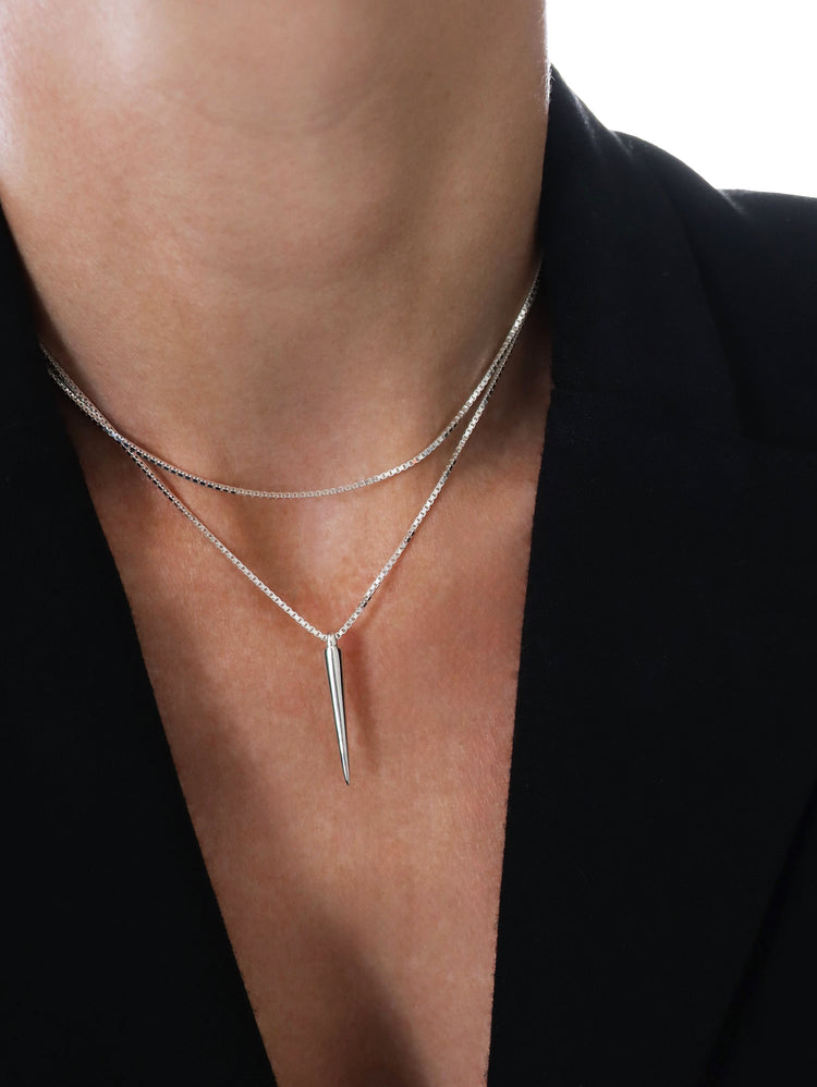 Kvinna som bär ett silverhalsband med en kedja som är virad två varv med ett hängsmycke som ser ut som en spik.