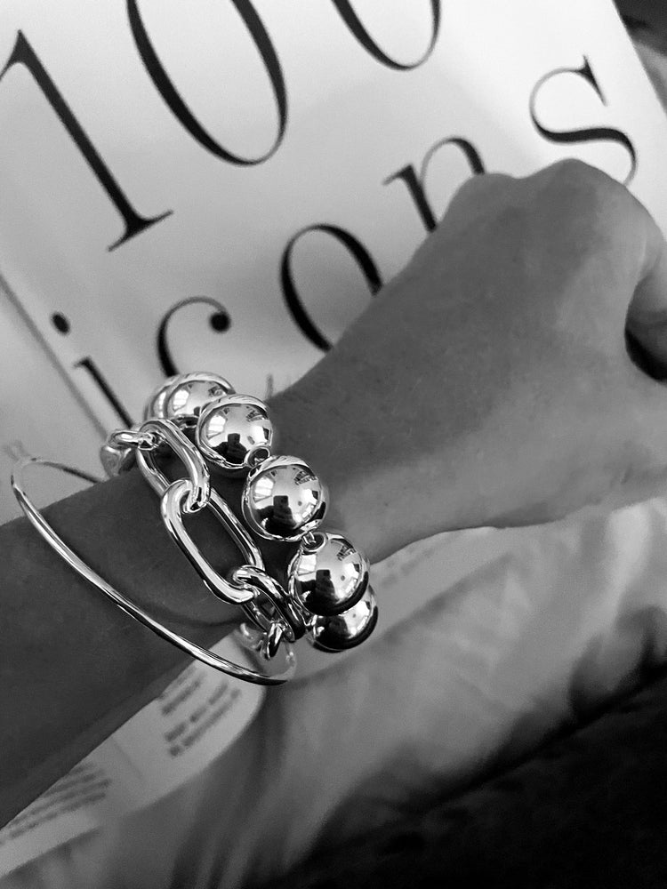 En tjej som bär flera stora silverarmband tillsammans. Ett brett silverarmband med stora kulor, en bred kedja och ett smalt stelt silverarmband.