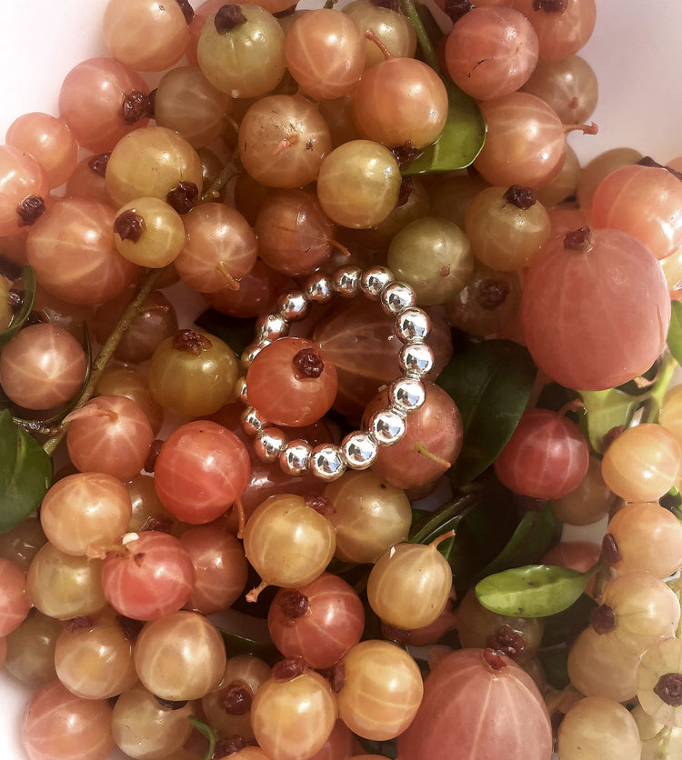 silverring med kulor placerad i en hög av vinbär.