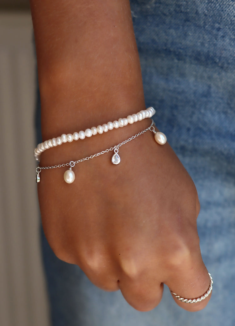 Tjej som bär armband med hängande pärlor och kristaller. Kombinerat med ett pärlarmband med små vita organiska pärlor.