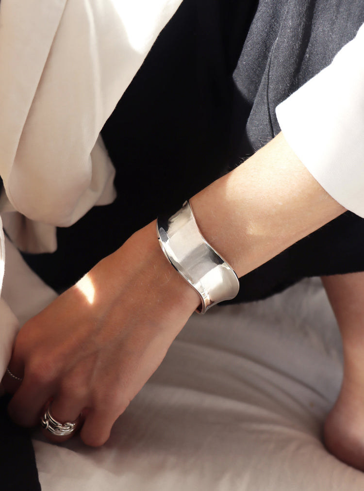 tjej som bär ett brett stelt silverarmband med vågig form.