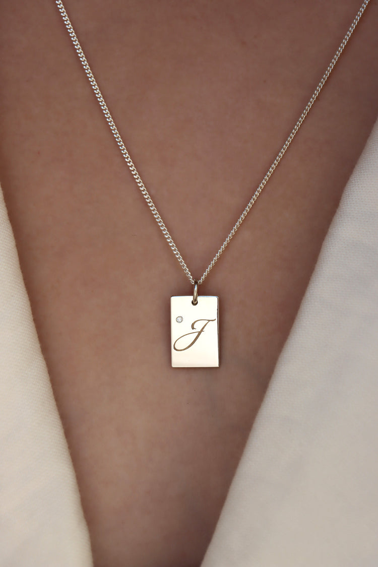 Tjej som bär ett halsband med bokstavsberlock i silver med liten diamant