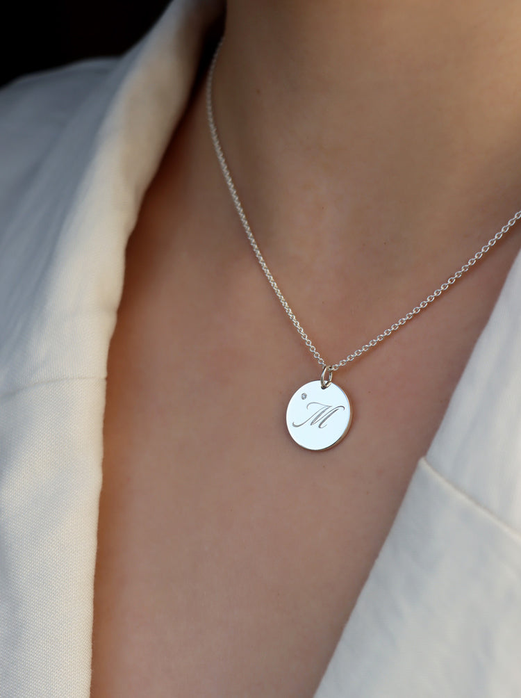 Tjej som bär ett halsband med bokstavsberlock i silver med graverat M och liten diamant