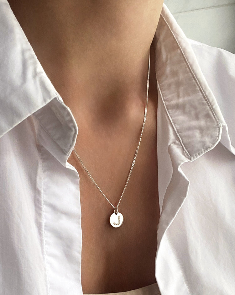 Kvinna som bär ett silverhalsband med berlock med diamantbokstav.