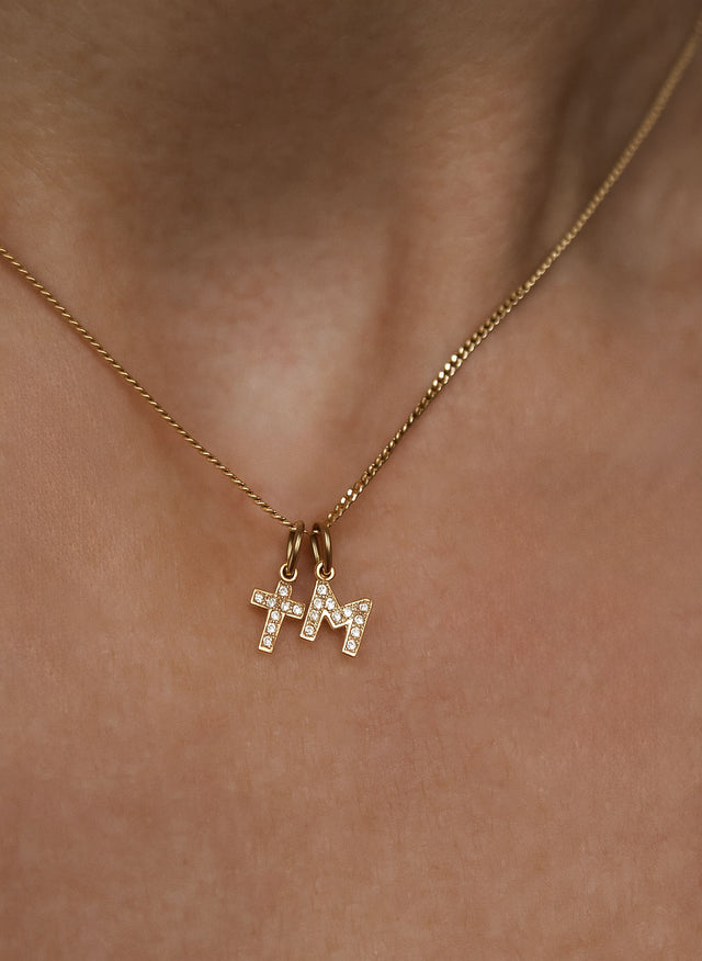 Kvinna som bär ett halsband med ett diamantkors i guld och en bokstavsberlock i guld med diamanter.