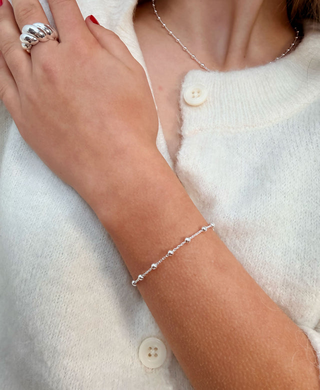 Tjej som bär ett smalt silverarmband med kedja och små kulor tillsammans med matchande halsband och en stor silverring.