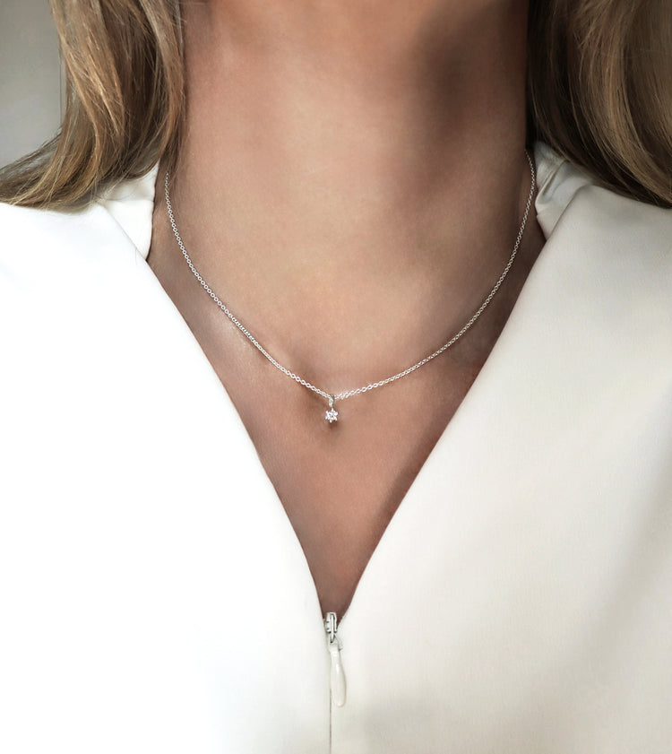 Halsband med liten diamant som bärs av en kvinna med vit klädsel.