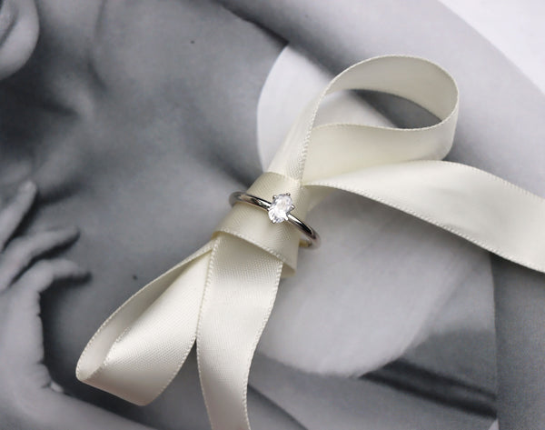 En diamantring med oval stor diamant placerad på en sidenrosett.