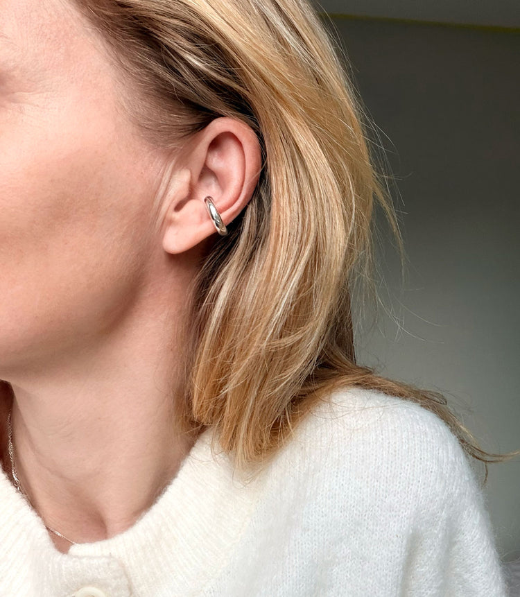 Tjej som bär en ensam ear cuff i örat. Ear cuffen är blank och i silver med tjocka former.