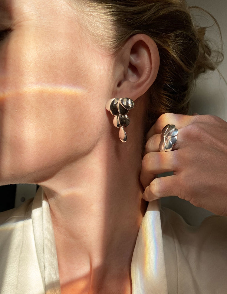 Modell som bär stora silverörhängen och silverring av samma design.