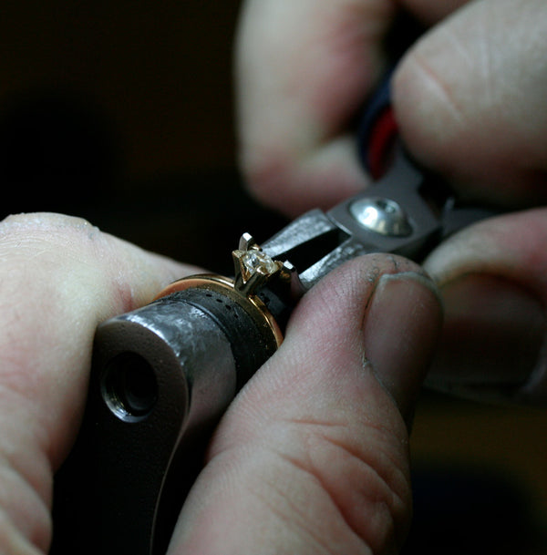En guldsmed som infattar en diamant i en guldring
