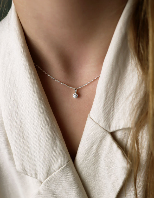 Diamanthalsband med hängsmycke och kedjan som bärs högt upp i halsen. Kvinnan bär vit kavaj.