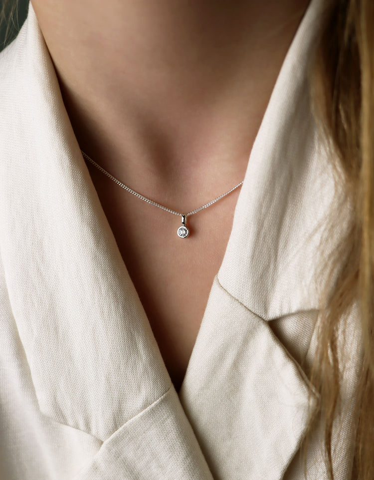 Diamanthalsband med hängsmycke och kedjan som bärs högt upp i halsen. Kvinnan bär vit kavaj.