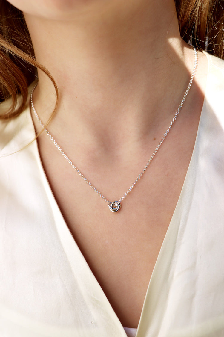 Tjej som bär ett silverhalsband med en liten knut.