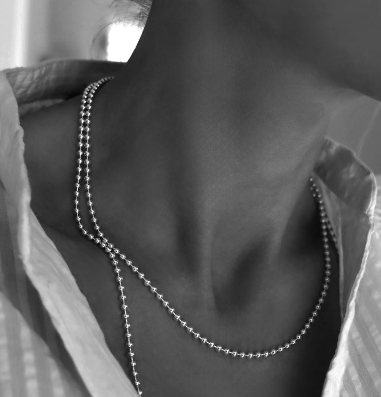 Kvinna som bär en kulkedja i silver, 3 mm bred, tillsammans med en längre kulkedja i silver.