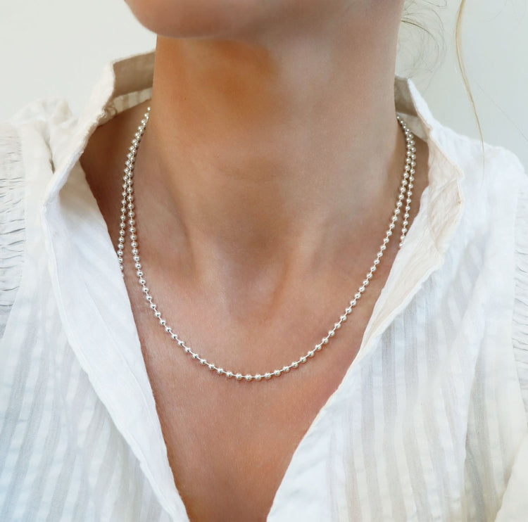 Tjej som bär ett halsband med en silverkedja som har små länkade silverkulor, 45 cm lång. hon bär vit topp.