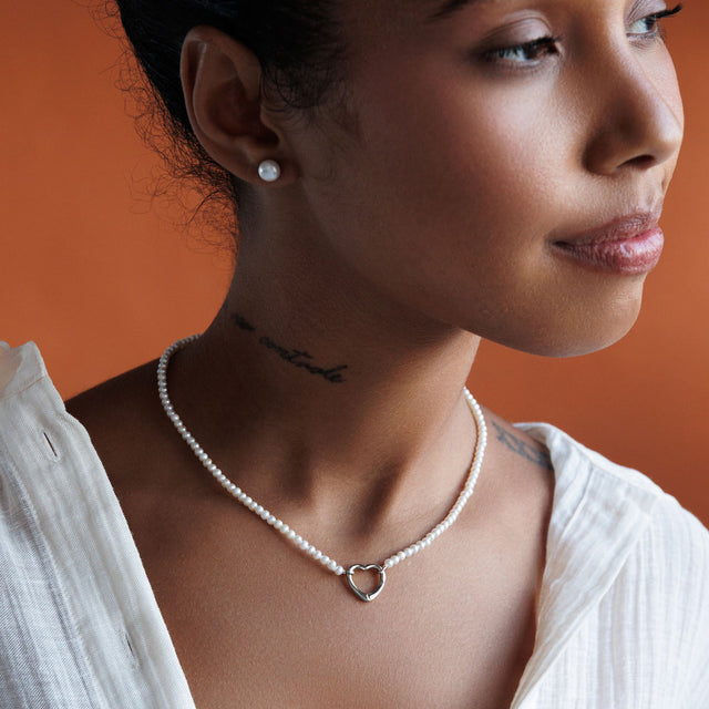 Tjej som bär ett pärlhalsband, kort choker halsband med vita små pärlor och hjärta i 925 silver.