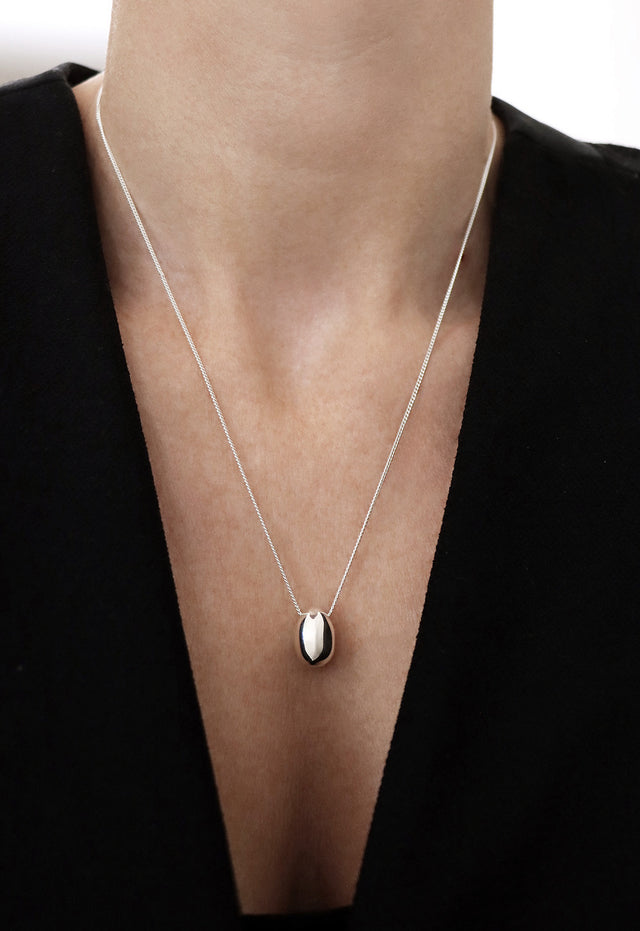 Kvinna som bär ett silverhalsband med ett äggformat hängsmycke i en silverkedja.
