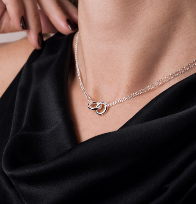 Kort silverhalsband med två ringar i kedjor på kvinna som bär svart sidentopp.