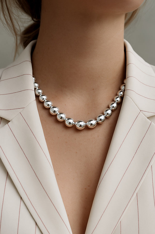 tjej som bär ett halsband med stora länkade silverkulor till vit kavaj .