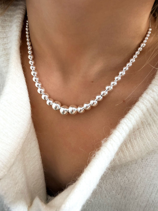 Tjej som bär ett kort silverhalsband med stora kulor.