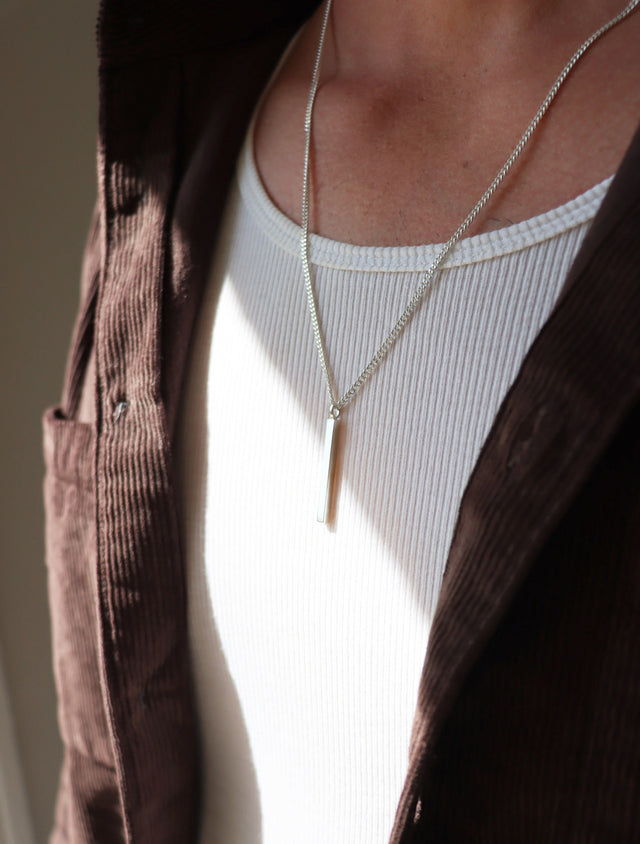 Man som bär ett långt silverhalsband med stav i kedja.