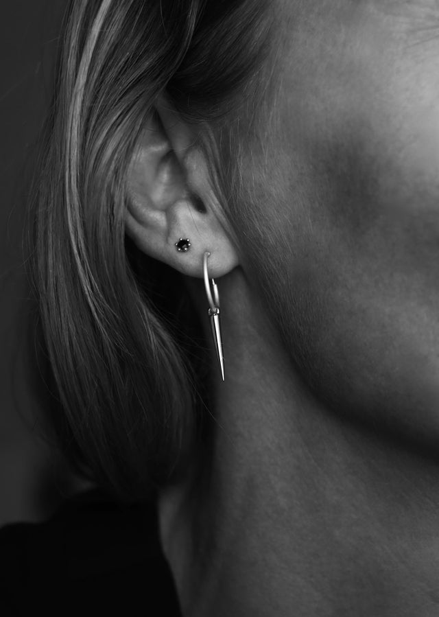 En kvinna som bär två örhängen i samma öra. Ett svart litet örhänge och ett silverörhänge med ring och berlock.