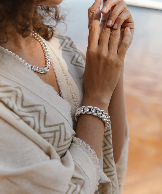 Kvinna på stranden som bär ett brett kedjearmband silver med matchande kedjehalsband
