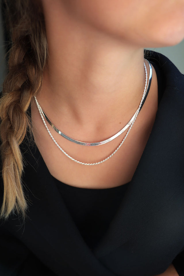 Tjej som bär en platt ormkedja, kort, kombinerat med en längre silverkedja.