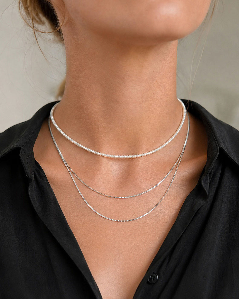 Tjej som bär halsband i lager på lager stil. Ett kort pärlhalsband av choker modell tillsammans med två silverkedjor i olika längder.