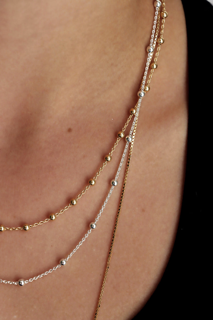 Tjej som bär flera tunna kedjor i silver och guld i olika längder.