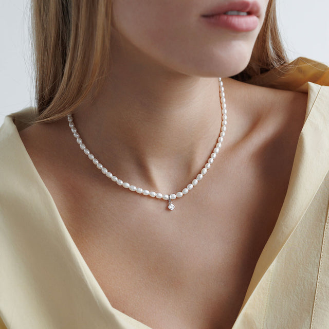 Tjej som bär ett pärlhalsband med små pärlor och berlock med kristall.