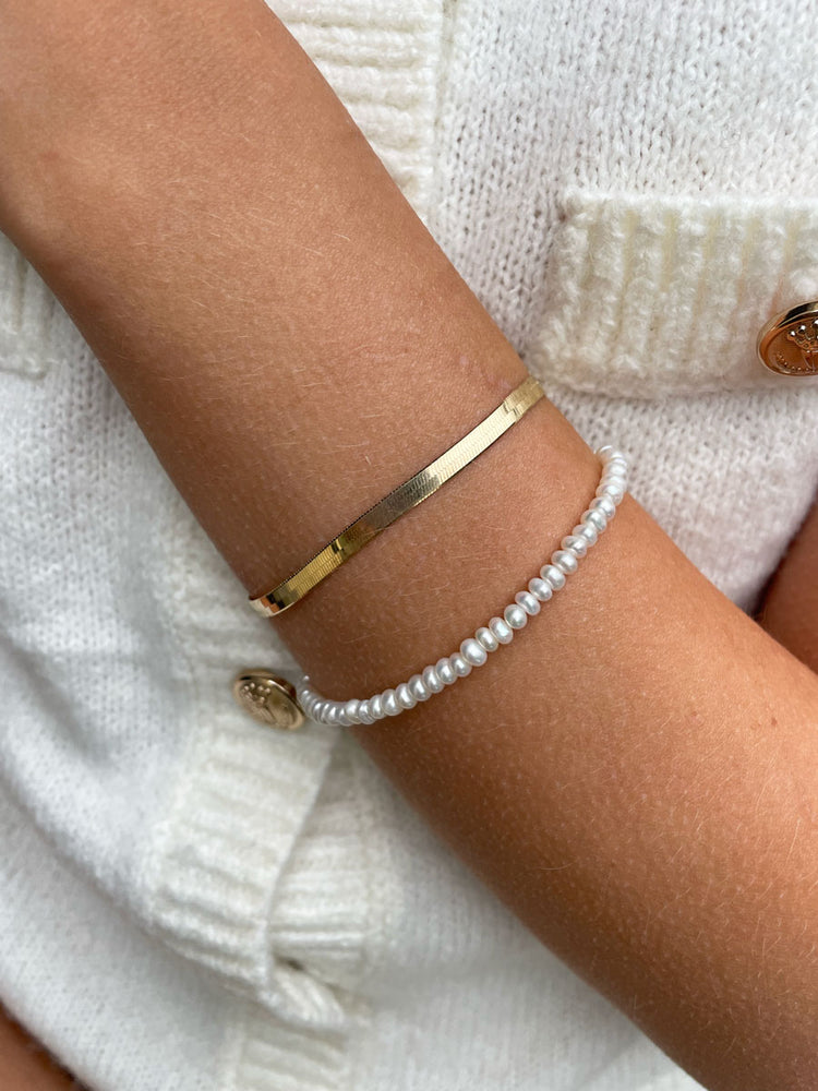 Tjej som bär ett pärlarmband med små pärlor, kombinerat med ett platt guldarmband.