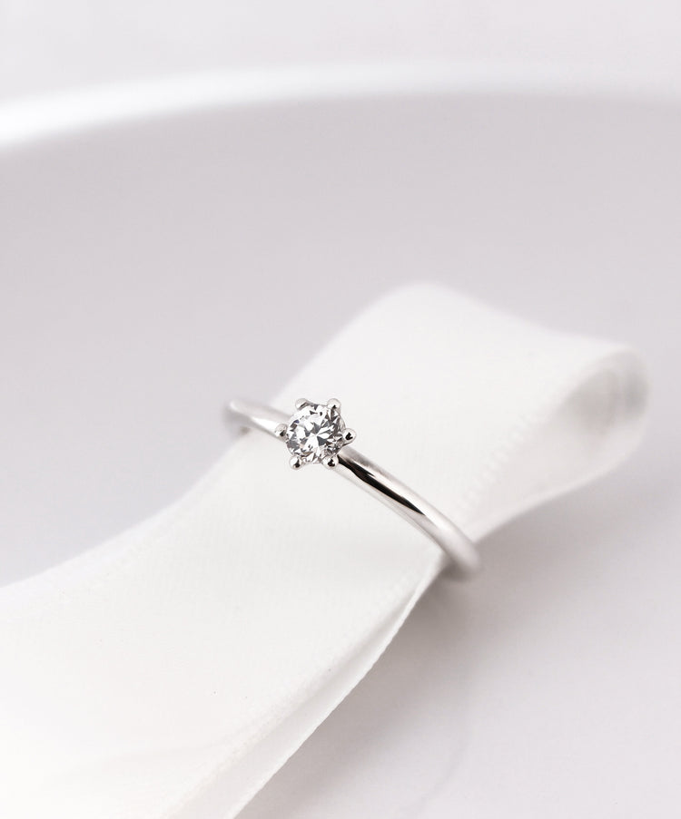Diamantring i silver med en briljantslipad 0,25 ct diamant placerad runt ett vitt sidenband.