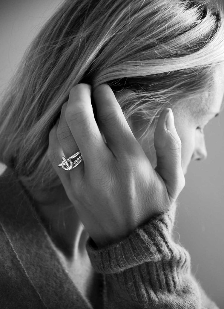 Kvinna som bär en silverring med knut i kombination med två smala ringar.