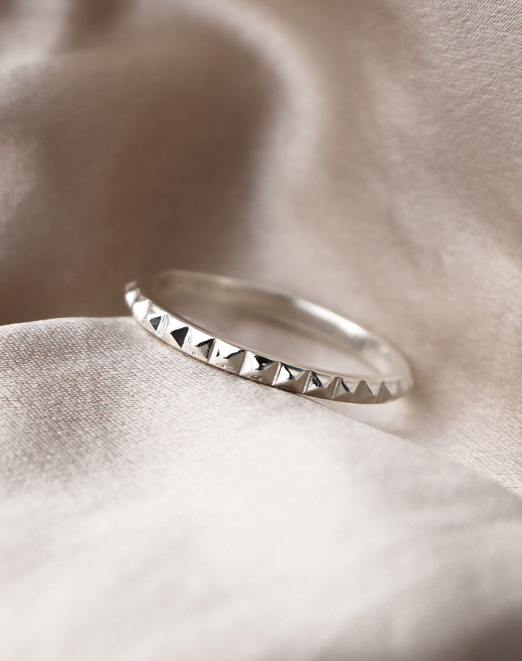 Silverring med nitar som ligger på ett sidentyg.