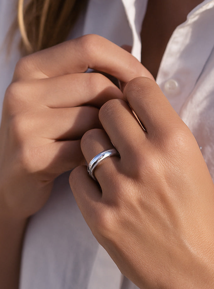 Tjej som bÀr en tjock silverring av blankt silver.
