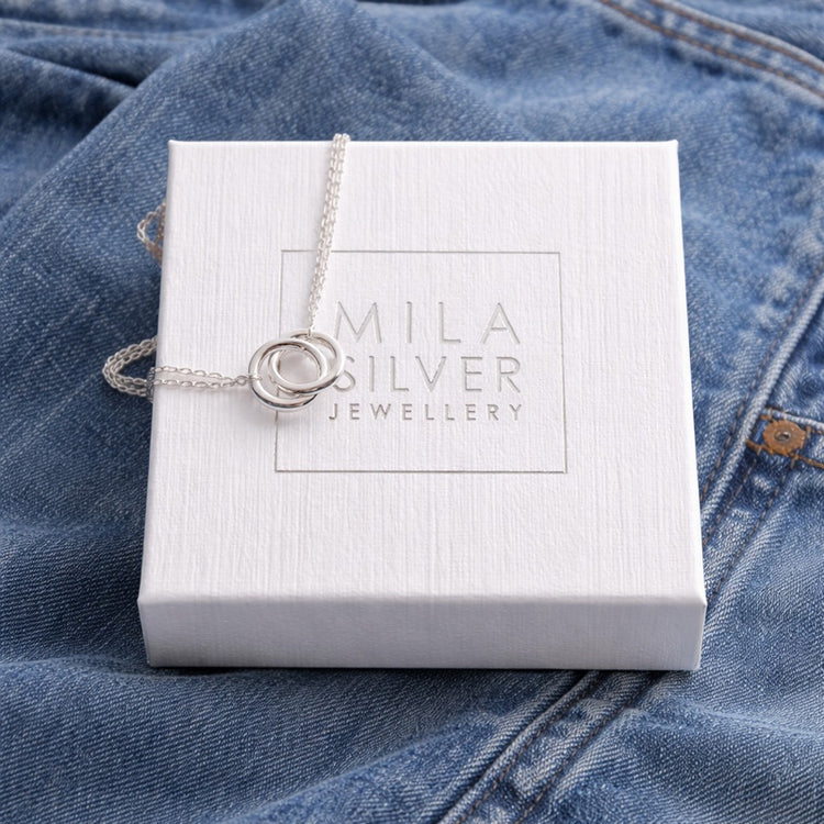Silverhalsband placerad på en vit ask från Mila Silver - ligger på ett par blå jeans.