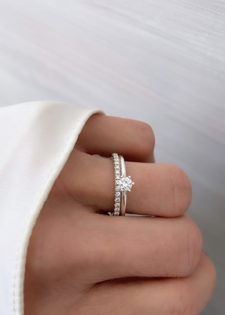 Kvinna som bär ett set med vigsel- och förlovningsring i silver. En alliansring med flera diamanter på rad och en solitärring med en 0,25 ct diamant.