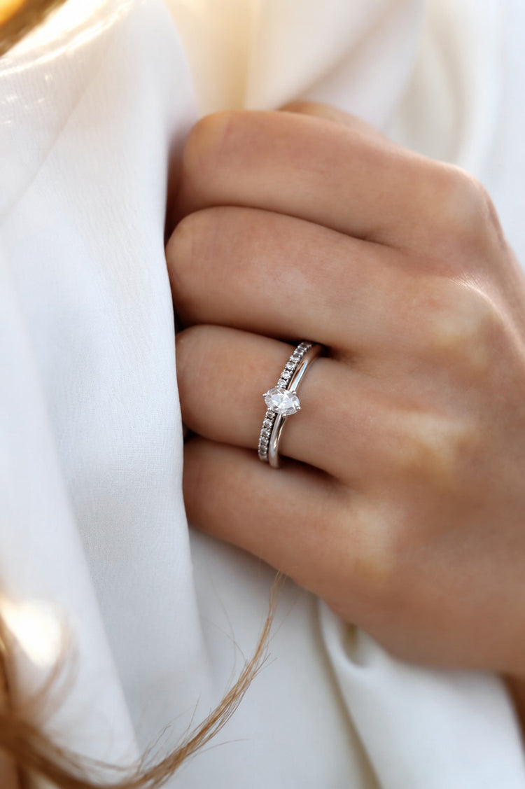 Tjej som bär ett set med förlovningsring med oval diamant och vigselring - alliansring. Ringar i 18k. vitguld med diamanter.