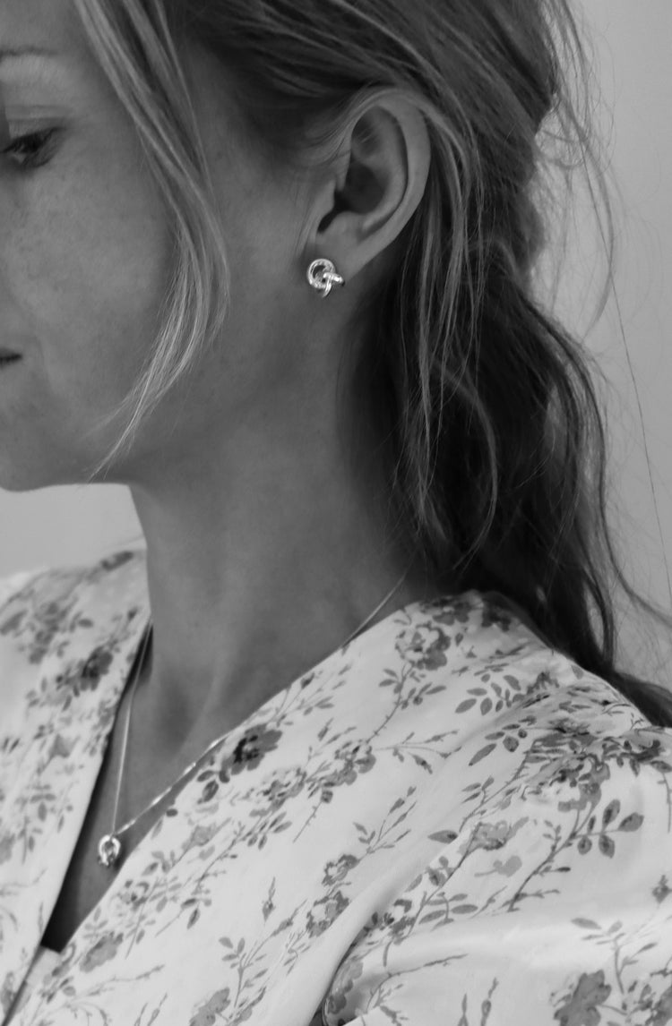 Tjej som bär örhängen med silverknutar och matchande halsband med knut.