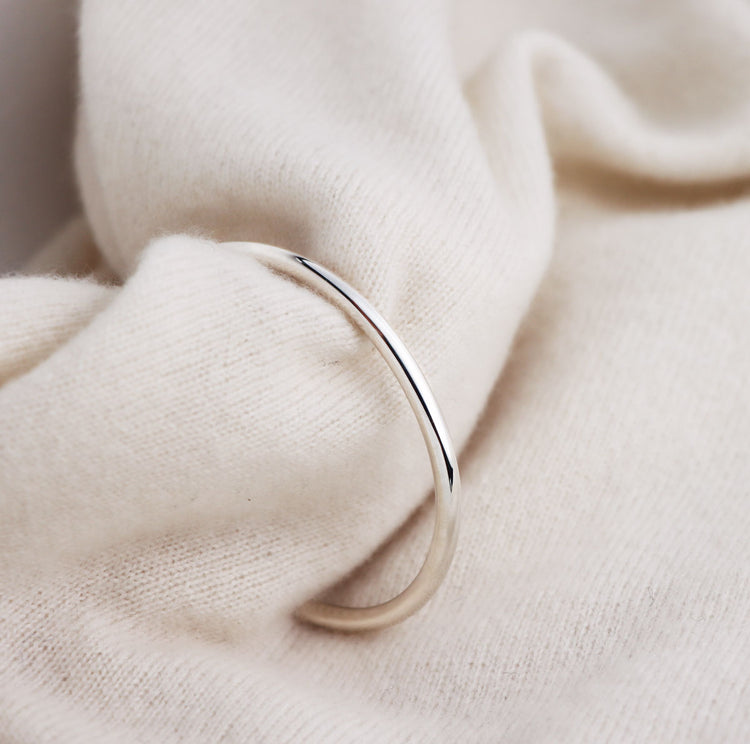 stelt silverarmband med blank yta som är placerat runt ett mjukt tyg.