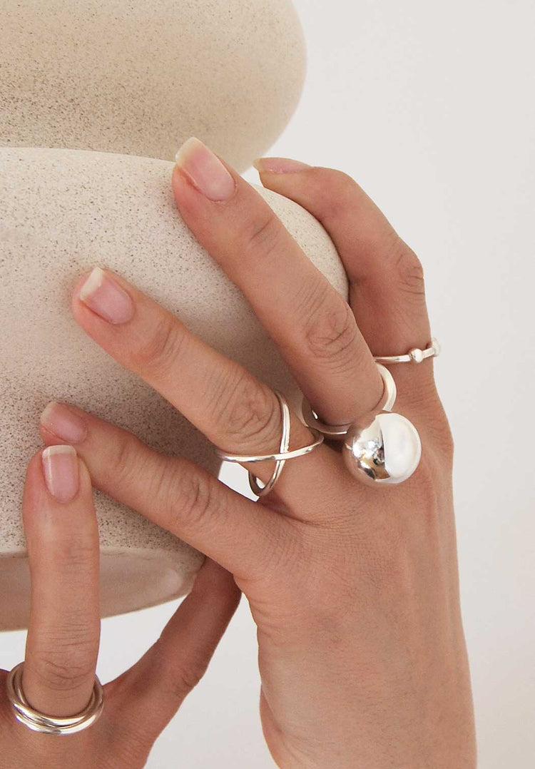 En hand med flera stora silverringar. A cross ring, Happy ring - en ring med stor kula och en smalare silverring.