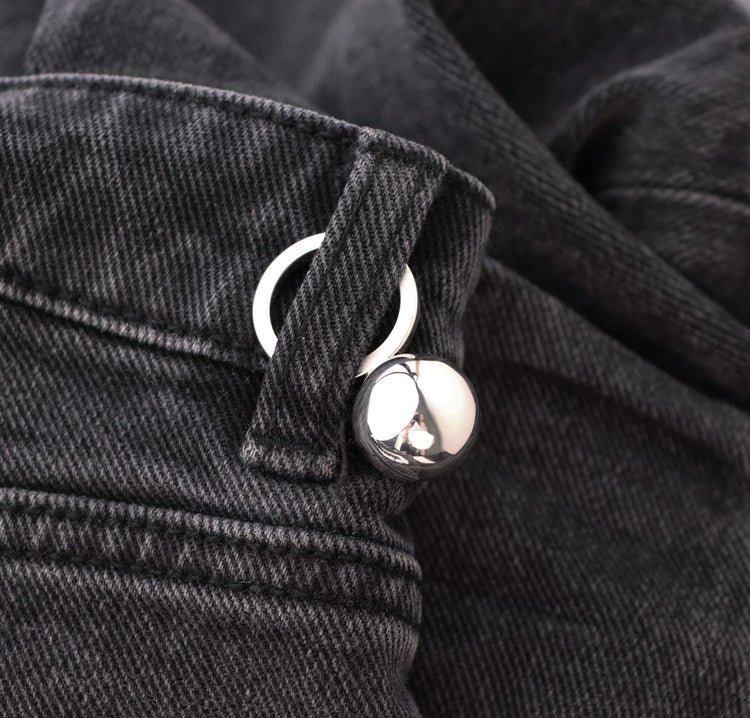 Silverring med en stor kula på toppen placerad på ett par svarta jeans.