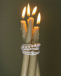 Tre levande ljus med pärlarmband som är virade runt ljusen. 