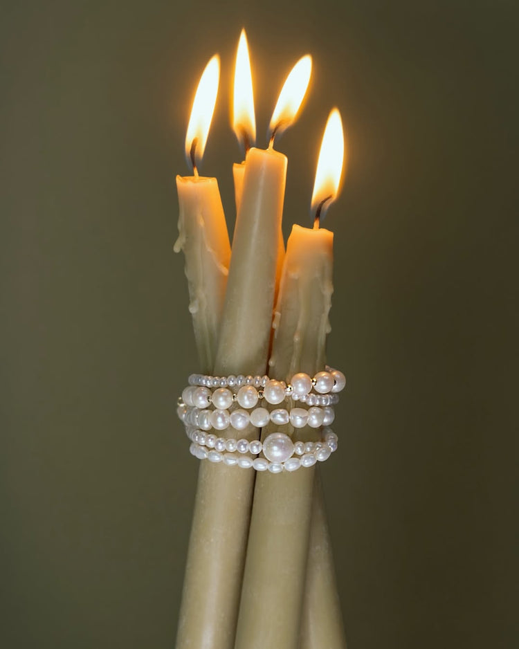 Tre levande ljus med pärlarmband som är virade runt ljusen. 