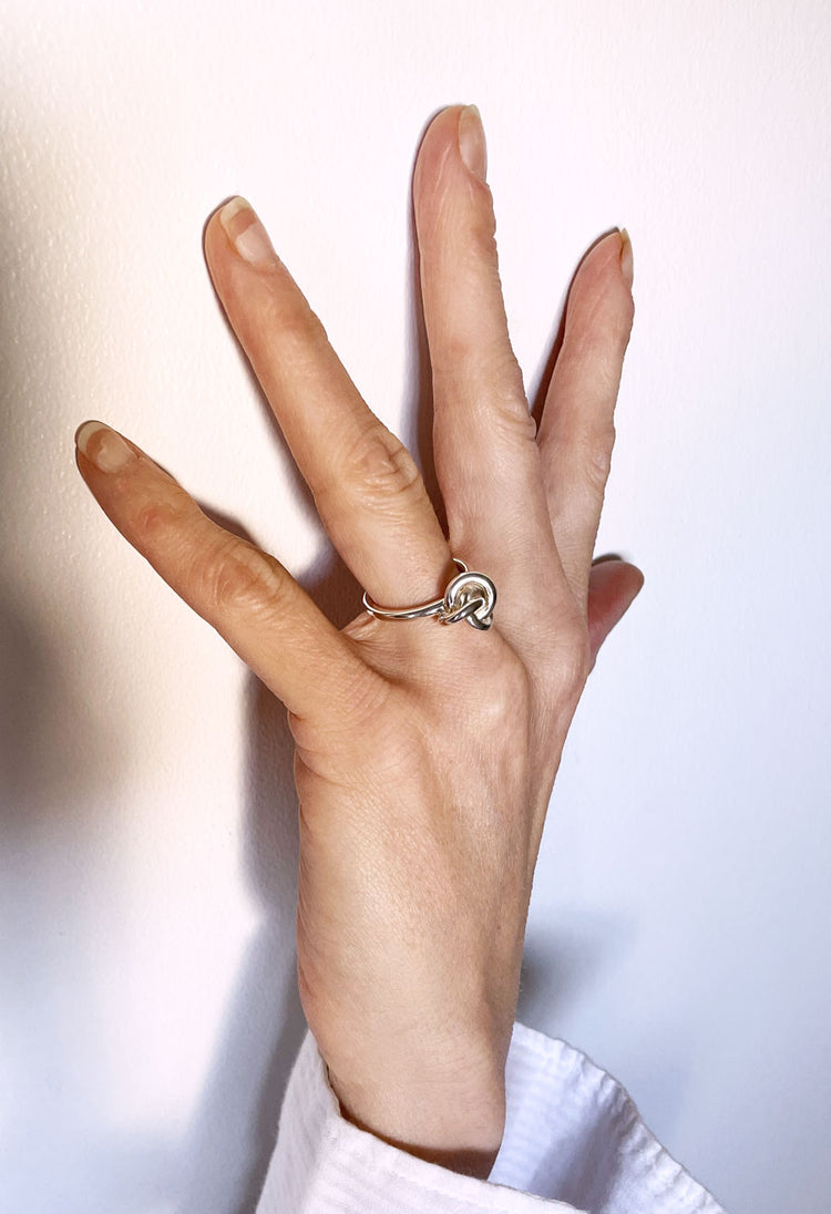 Hand med en silverring med knut som poppar på handen. 