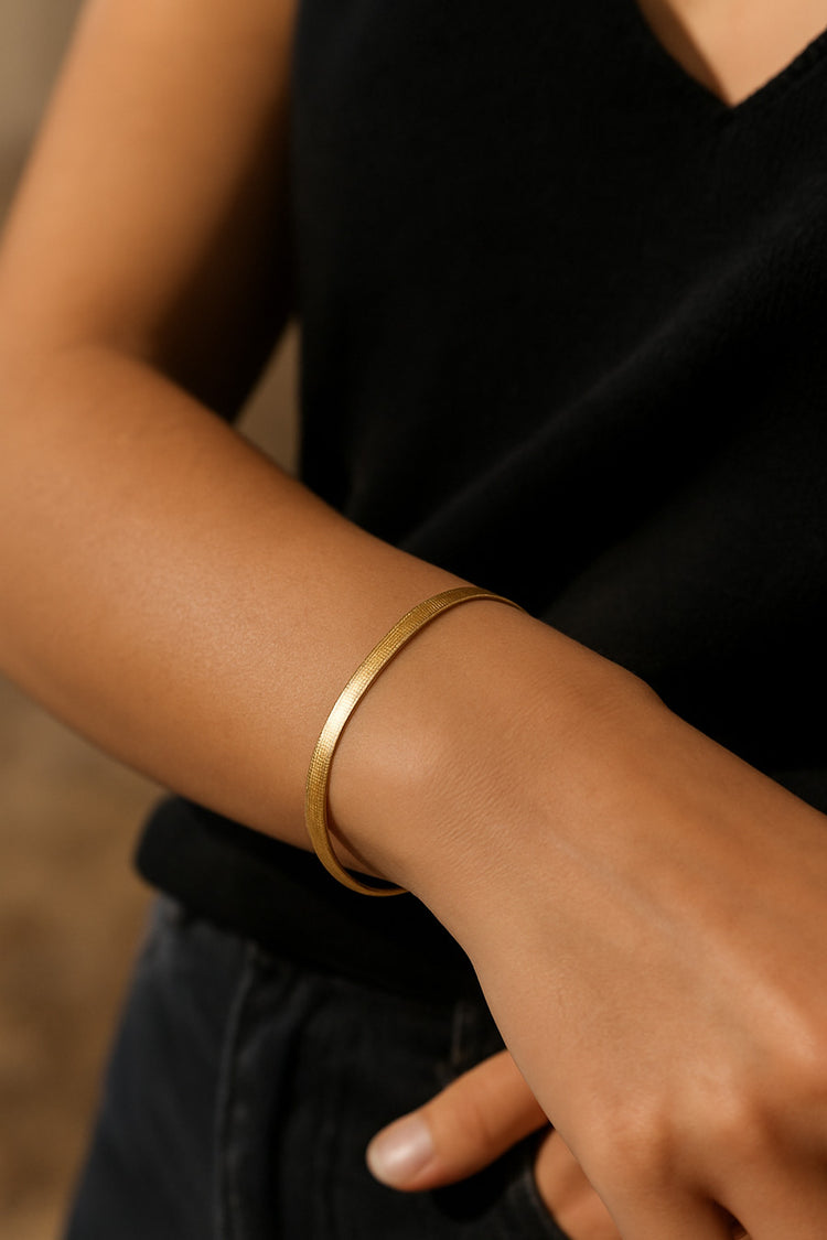tjej som bär ett armband med platt snakekedja i guld. 