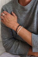 Man som bär ett smalt silverarmband med repkedja, kombinerat med svart stenarmband och silverring. 