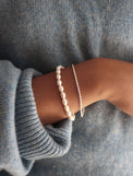 Tjej som bär ett smalt pärlarmband kombinerat med silverarmband. 